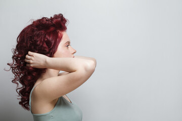 Obraz premium Beautiful woman touching her red curly hair against white studio wall background