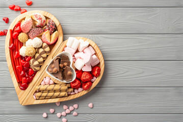 Valentine's Day concept. Top view photo of wooden heart shaped serving tray with sweets plate chocolate jelly candies and cookies on grey wooden desk background with blank space