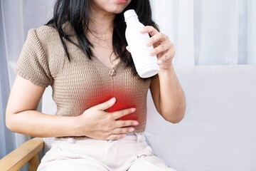 Asian woman taking antacid medicine gel to treat her heartburn from gerd and stomachache