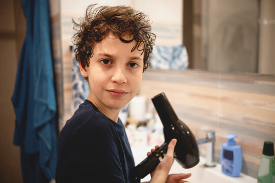 A Child Dries His Hair In The Bathroom Holding Hair Drier