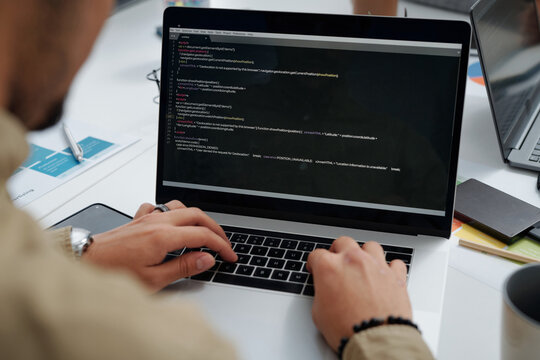Close-up of young developer writing codes on computer while working at table at IT office