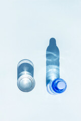 Bottled water. A bottle of mineral water and glass of water with hard shadows on blue background....