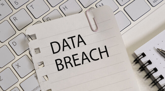Data Breach text on paper lying on the keyboard with a notepad and a pen