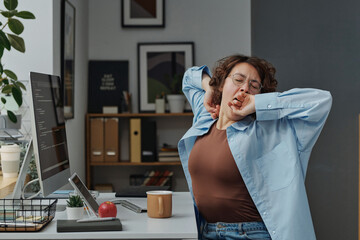 Young businesswoman tired of her sitting work at computer, she sitting at workplace and yawning