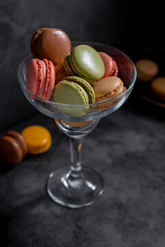 Macaroons colorful cookies in glass, moody dark background. Macarons french sweet dessert, pink background.