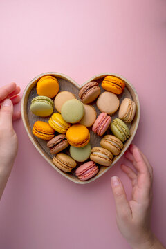 Macaroons colorful cookies in wooden heart bowl. Macarons french sweet dessert, top view, pink background. Copy space