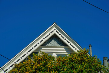 Double gable roof facade with decorative exterior and white accent paint on edge of tiles and front yard tree with dark blue sky