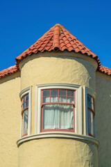 Spire or turrent on a house or building with red adobe roof tiles and beige stucco exterior with white accent paint windows.
