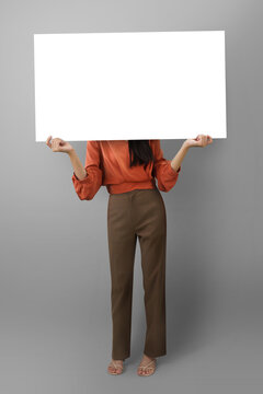 Woman holding white landscape blank poster on grey background. mockup for design.