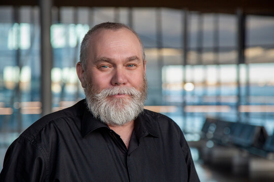Portrait of a bearded middle-aged man. Happy senior man 50 55 60 years old with gray beard at the airport, office, indoors background looking at camera. Older man traveling concept