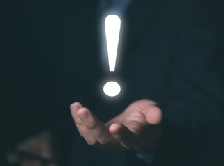 The businessman's hand shows a white exclamation mark.	