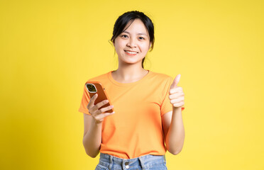 image of asian girl holding phone and isolated on yellow background