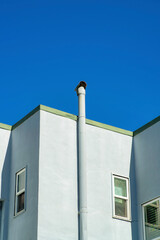 Gray blue stucco house with large metal chimney vent and flat roof with windows in view on home or house in the neighborhood