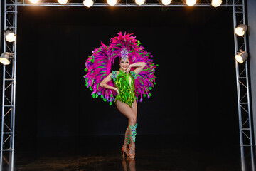 A young girl dancer of European appearance on stage in a carnival costume of green and pink feathers