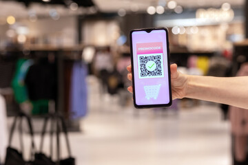 Close-up of women's and showing smartphone with purchases in online store. Scan qr code for discount coupon. Defocused shop at background. Concept of shopping and consumerism