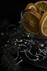 on a dark background and on a black tray stands a transparent glass with dry oranges and a branch of a Christmas tree and garlands on top of a little snow. for screensavers, postcards, labels, invitat