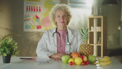 A female doctor sitting with different types of fruits on the desk whiling looking and smiling at camera - Powered by Adobe