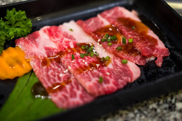 Premium raw Japanese beef sliced with sauce and sprinkle with white sesame seeds and sliced spring onions on black tray