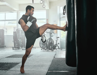 Male athlete kicking a punching bag in a gym while practicing, training and fitness exercise....