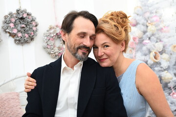 Portrait of positive elegant couple resting at home. Relaxed man keeping his eyes closed and feeling pleased while being embraced by his charming calm woman