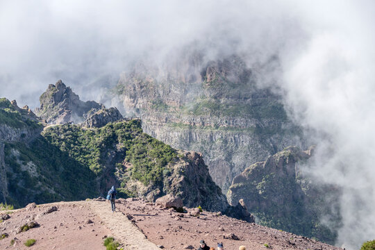 walking on path with volcanic slopes looming out of clouds, north of Miradouro de Areeiro peak, Madeira