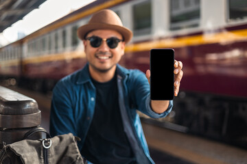 Traveler young asian man using cellphone booking trip at terminal train station. Happy tourist travel by train using smartphone searching location. Male Backpacker arrival at platform railway.