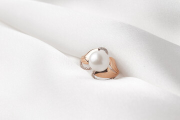 Pearl ring with golden fittings on shiny white silk background. Beautiful accessories for women....