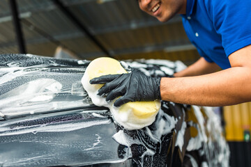 Man worker washing car service with foam and sponge. Car wash cleaning wipe station. Employees...