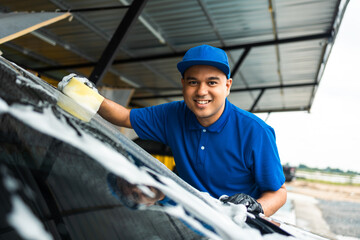 Man worker washing car service with foam and sponge. Car wash cleaning wipe station. Employees clean a vehicle professionally.
