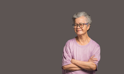 Beautiful elderly Asian woman looking at the camera with a smile while standing on a gray background