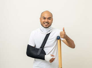 Happy young asian man broken arm and leg on isolated. Man put on plaster cast splint with walking...