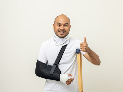 Happy young asian man broken arm and leg on isolated. Man put on plaster cast splint with walking sticks crutches. Patient wearing sling support arm with neck collar. life insurance and accident