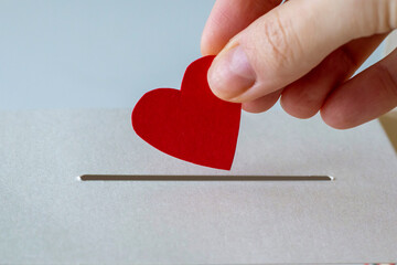 The concept of donations. A woman's hand places her heart in a slit of a box in close-up.