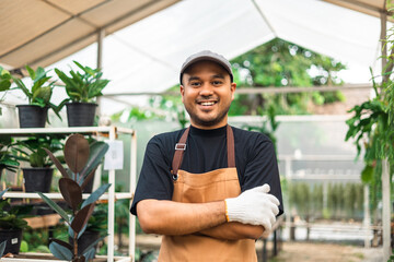 Happy gardener man in gloves and apron plants flowers in greenhouse. Florists man working gardening...