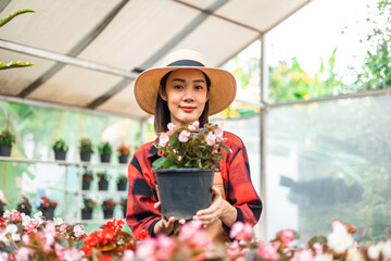 Happy gardener woman in gloves plants flowers in greenhouse using tablet check growth quality of Plant. Florists woman working gardening in the backyard. Flower care harvesting.