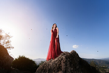 Chica joven con vestido rojo en zona boscosa y castillo medieval posando