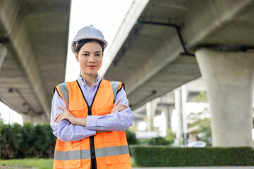 Asian engineer worker woman or architect looking construction with white safety helmet in construction site. Standing at highway concrete road site. Progress planning of highway bridge.