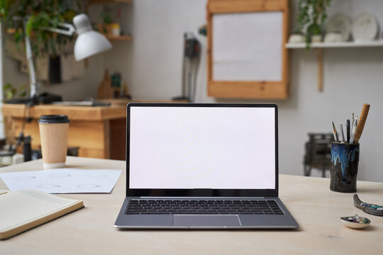 Background image of open laptop with white screen mock up at desk in creative studio, copy space