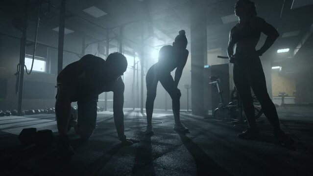 exhausted bodybuilders in dark gym, silhouette of male and female sportspersons, people are resting