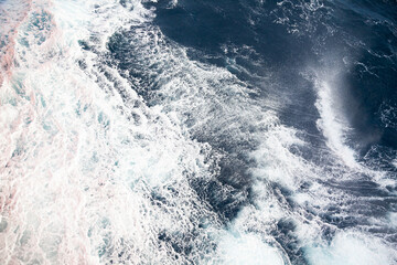 Fototapeta na wymiar Rushing water in the open sea. Blue water background with white foam.