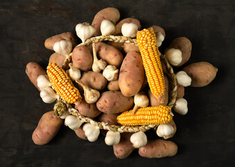 a pile of potatoes, corn cobs and garlic, still life on a dark wooden background