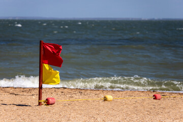 Yellow-red flags of rescuers on the city sandy beach separate the bathing areas and prohibit...