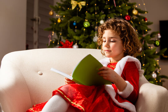 Beautiful little girl sits on the chair next to a nicely decorated Christmas tree