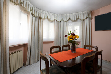 Living room of a house with a corner dedicated to a dining room with a wooden table and six matching chairs in a semicircular room