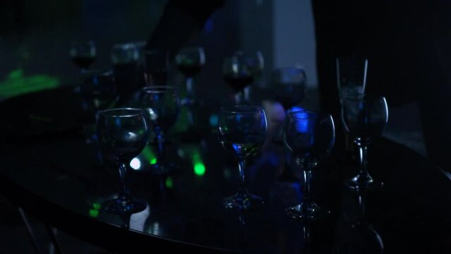 Lots of wine glasses and drinks on the table in a dark club, people dancing and having fun in the background