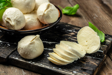 fresh handmade soft Italian cheese with fresh basil leaves from Puglia, white balls of burrata or burratina cheese made from mozzarella and cream filling on a wooden board - obrazy, fototapety, plakaty