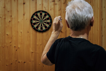 A man with gray hair plays darts. Rear View Of Man Playing Darts.