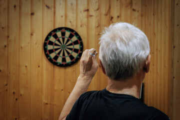 A man with gray hair plays darts. Rear View Of Man Playing Darts.