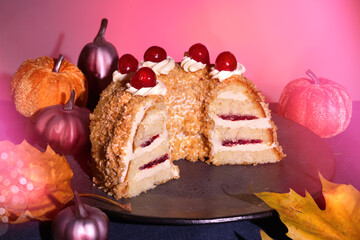 German cake Frankfurter Kranz or Frankfurt Crown Cake. Bisquit with butter cream and cherries. Cut half of the cake. Autumn decor with textile pumpkins and dry leaves.