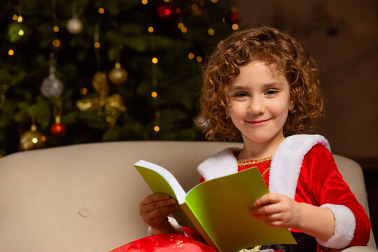 Beautiful little girl sits on the chair next to a nicely decorated Christmas tree